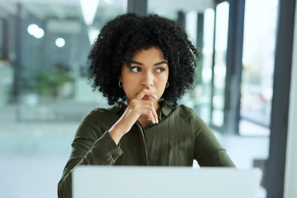 Photo d'une jeune femme devant un ordinateur en proie à ses doutes, elle pourrait être aidée par des séances de coaching pour repérer ses blocages et paternes. gestion du stress – Audrey Martin Coaching – accompagnement individuel ou collectif